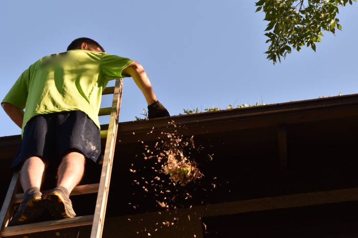 man on ladder cleaning leaves from gutter